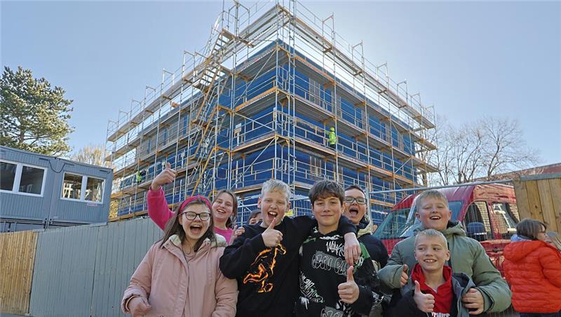 Gruppe von Menschen vor einem mehrstöckigen Gebäude mit Gerüst und blauer Verkleidung im Freien