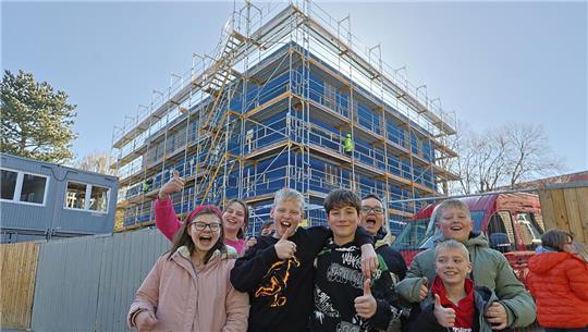 Gruppe von Menschen vor einem mehrstöckigen Gebäude mit Gerüst und blauer Verkleidung im Freien