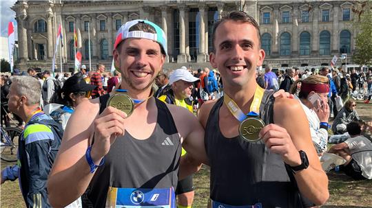 Dean Sauthoff (r.) und Dominic Sswat präsentieren vor dem Reichstag ihre Finisher-Medaille des 50. Berlin-Marathons. 58.212 Läuferinnen und Läufer sind zur Jubiläumsausgabe am Start, so viele wie nie zuvor.