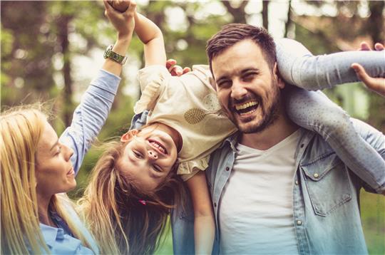 Frau und Mann albern mit ihrer Tochter und lachen in die Kamera.