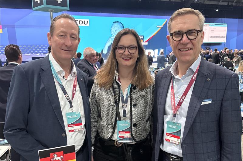 Zwei Männer und eine Frau stehen nebeneinander und blicken in die Kamera.