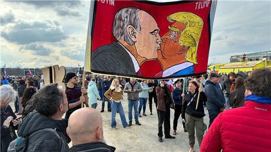 Demonstranten halten bei einer Kundgebung des Bündnisses „Eine Million Augenblicke für Demokratie“ ein Banner, auf dem sich stilisiert US-Präsident Trump und Russlands Präsident Putin küssen.