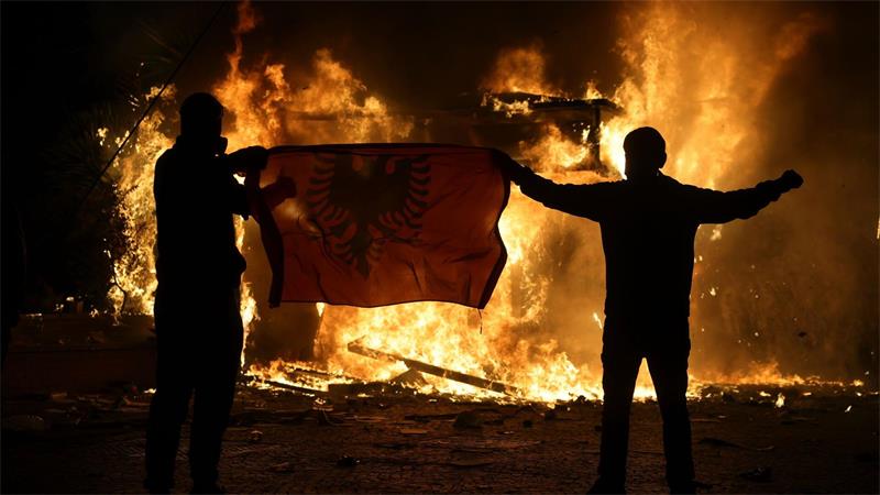 Demonstranten halten während Ausschreitungen in Tirana eine albanische Fahne vor einem brennenden Tabakladen hoch, als sich Studenten einer regierungsfeindlichen Demonstration anschließen.