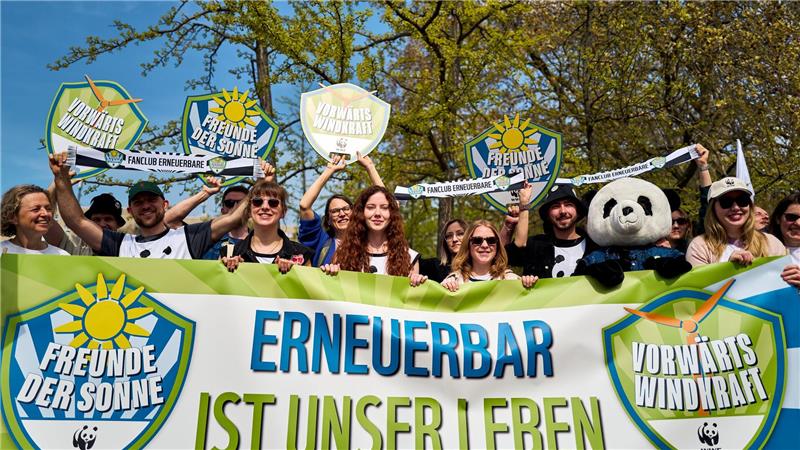 Demonstrierende halten ein Banner und Schilder in die Höhe, darunter eine Person im Pandakostüm.