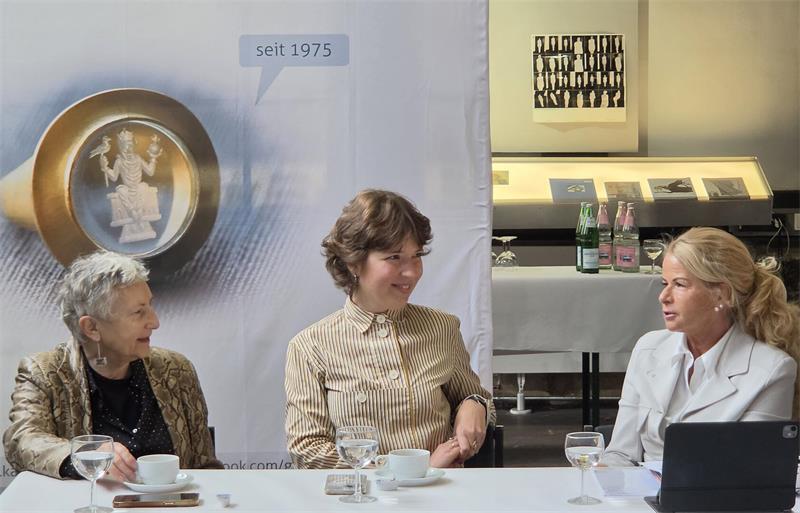 Drei Frauen bei Kaffee und Wasser an einem weißen Tisch im Gespräch. 
