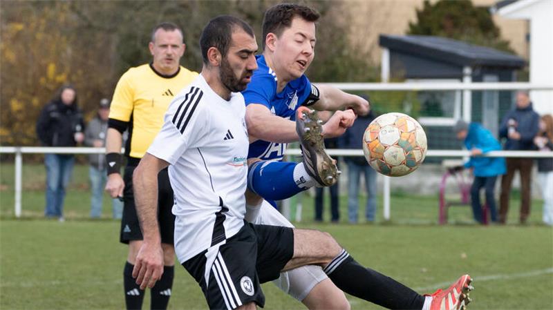 Zwei Spieler, einer im weißen Trikot, einer im blauen Trikot, kämpfen um den Ball.