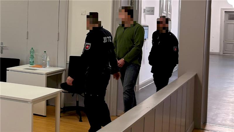 Zwei Justizmitarbeiter führen den 47-jährigen Mann an Handschellen in den Gerichtssaal.