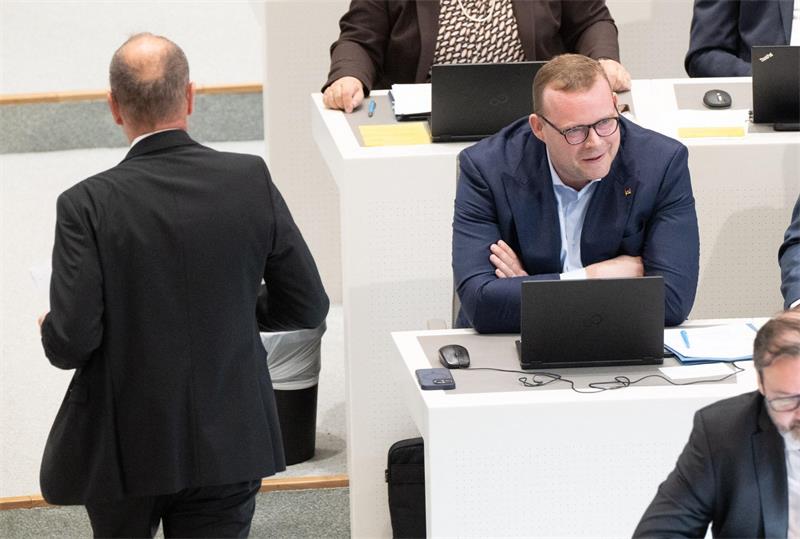 EIn Mann stützt sich mit seinem Oberkörper auf einem Tisch ab, vor ihm steht ein aufgeklappter Laptop