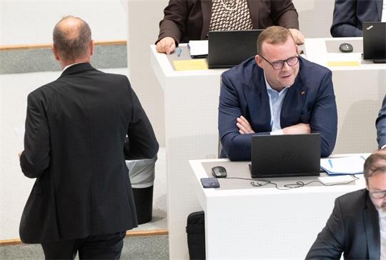 EIn Mann stützt sich mit seinem Oberkörper auf einem Tisch ab, vor ihm steht ein aufgeklappter Laptop