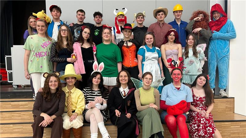 Gruppenfoto von Jugendlichen in verschiedenen Kostümen, darunter ein Harry-Potter-Outfit, ein Häschenkostüm und ein rotes Krabbenkostüm, auf einer Treppe in einem Innenraum.