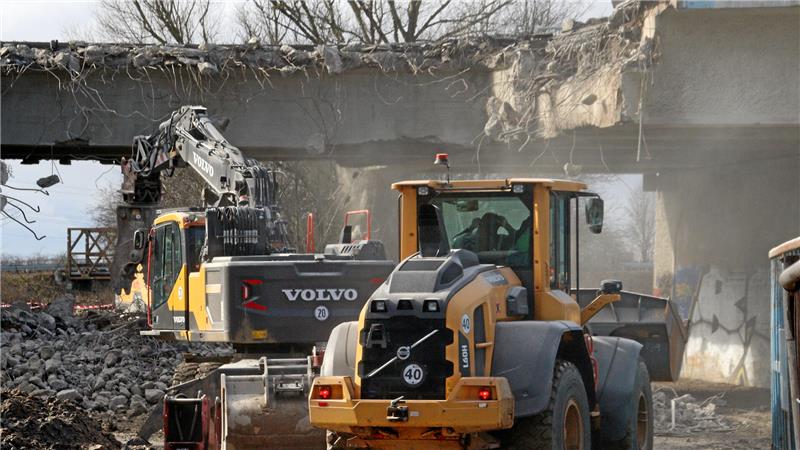 Baufahrzeuge beim Brückenabriss, über sie erhebt sich eine Staubwolke.