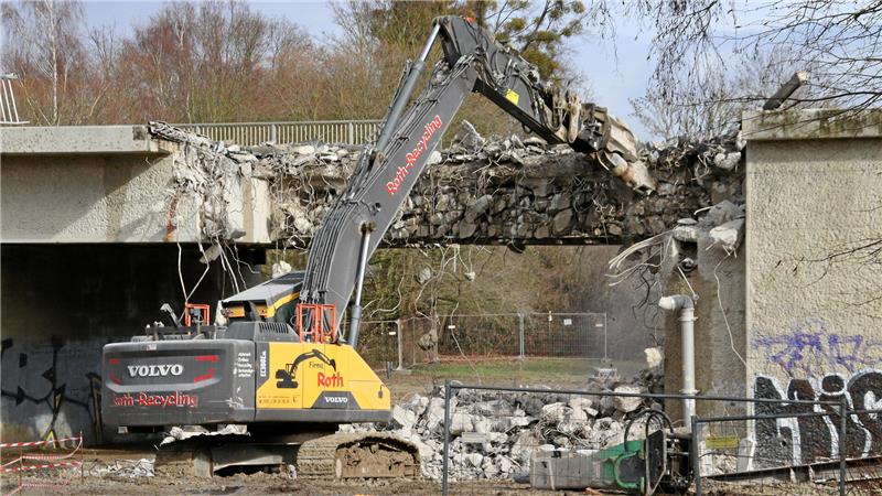 Ein Abbruchbagger knabbert an einer Brücke.
