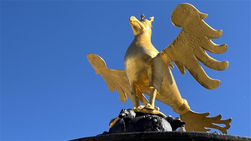 Goldene Adlerstatue mit ausgebreiteten Flügeln vor blauem Himmel