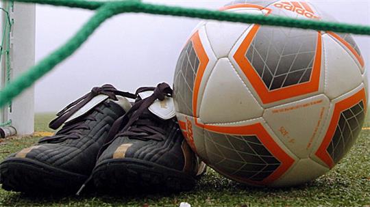 Fußballschuhe und ein Adidas-Fußball liegen auf dem Rasen hinter dem grünen Tornetz