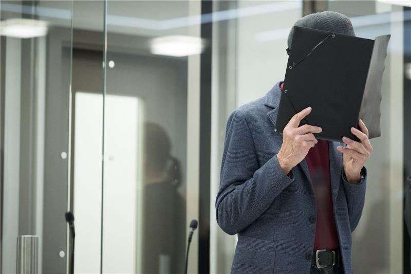 Mord aus dem Hinterhalt: Ex-Stasi-Mitarbeiter bestreitet Tat Der Angeklagte hält sich zu Beginn des Prozesses eine Mappe vors Gesicht. Der 80-Jährige will sich zu den Vorwürfen nicht äußern.