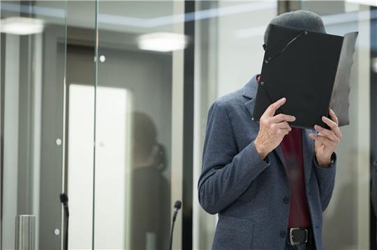 Der Angeklagte hält sich zu Beginn des Prozesses eine Mappe vors Gesicht. Der 80-Jährige will sich zu den Vorwürfen nicht äußern.
