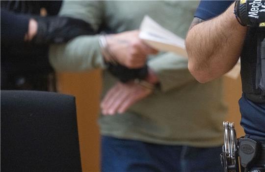 Der Angeklagte (m.) wird in Handschellen in einen Saal des Oberlandesgerichts Stuttgart geführt.
