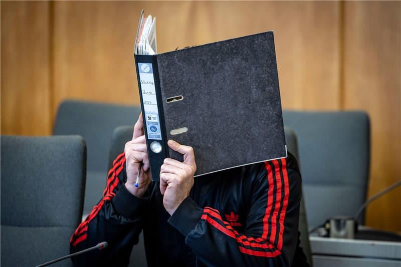 Polizist überfahren und mitgeschleift: 13 Jahre Haft Der Angeklagte verbirgt im Landgericht sein Gesicht hinter einem Aktenordner.