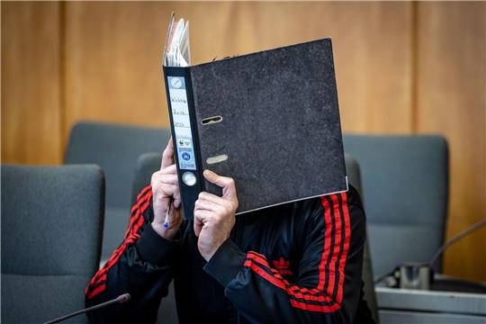 Der Angeklagte verbirgt im Landgericht sein Gesicht hinter einem Aktenordner.