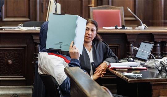 Der Angeklagte verbirgt zu Prozessbeginn sein Gesicht hinter einem Aktenordner. Er soll seine im Rollstuhl sitzende Großmutter getötet haben.