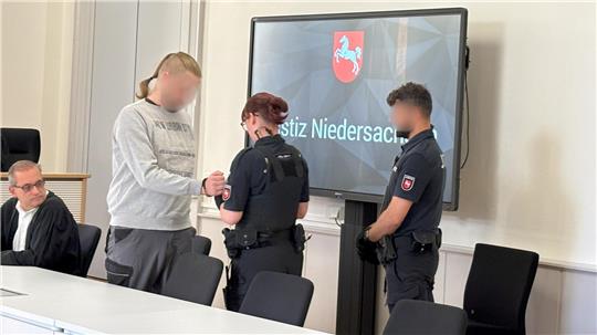 Der Angeklagte wird im Gerichtssaal von den Handschellen befreit. Links sein Verteidiger Claus Mielke.