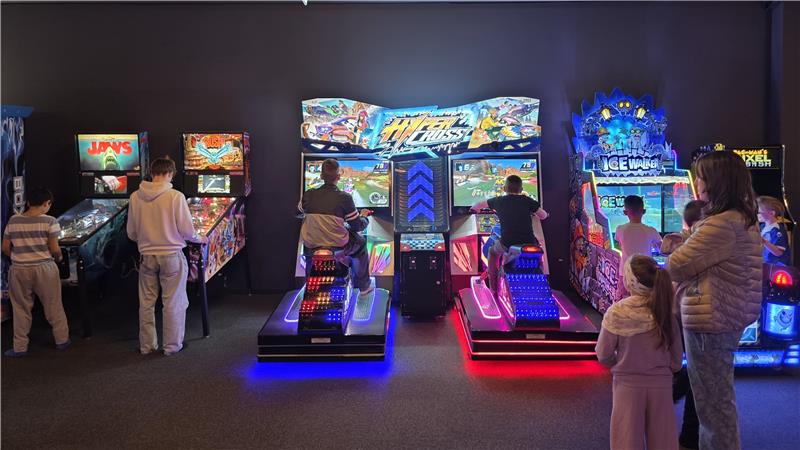 Mehrere Personen spielen an beleuchteten Arcade-Automaten in einem dunklen Raum.