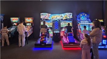 Mehrere Personen spielen an beleuchteten Arcade-Automaten in einem dunklen Raum.