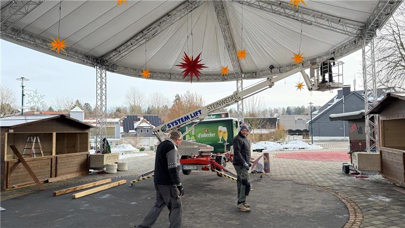 Das Foto zeigt einen Mann, der von einem Hubwagen aus Lichter an einem großen Zeltdach anbringt. Außerdem gehen zwei Handwerker über einen Platz.