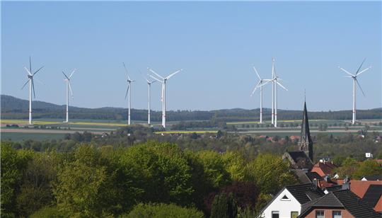 Im Hintergrund ein Windpark, im Vordergrund ein Dorf mit Kirchturm.