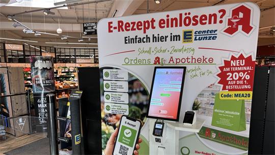 Aufsteller im Supermarkt mit Werbung für das Einlösen von E-Rezepten im Edeka-Center Lunze und einem Terminal mit Touchscreen