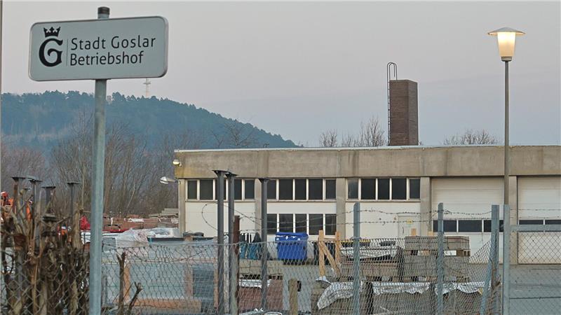 Gelände mit Zaun, Laterne und einem Schild mit der Aufschrift 'Stadt Goslar Betriebshof' vor einem flachen Gebäude und bewaldetem Hügel im Hintergrund