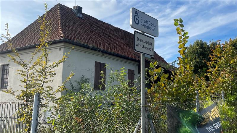 Ein weißes Haus mit rotem Ziegeldach hinter einem Zaun, davor ein Straßenschild mit dem Text 'Stadt Goslar Betriebshof' und 'Dieses Obejkt wird überwacht'.
