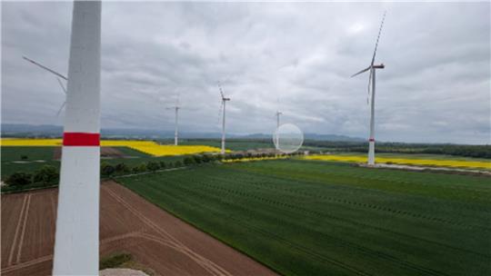 Mehrere Windräder stehen auf Feldern unter bewölktem Himmel