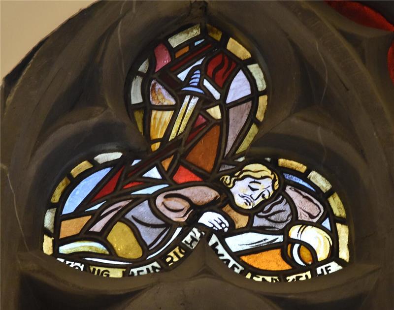 Buntes Kirchenfenster mit einer Darstellung eines schlafenden Menschen und einem Schwert