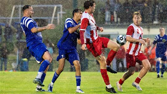 Fußballspieler in blauen und rot-weißen Trikots kämpfen bei Regen um den Ball auf dem Spielfeld
