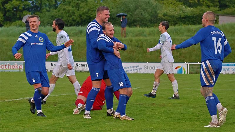 Fußballspieler in blauen und weißen Trikots auf einem Spielfeld mit grüner Wiese und Bäumen im Hintergrund.