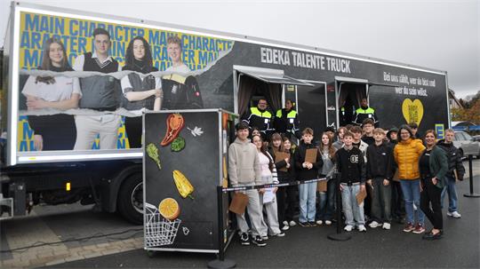 Gruppe von Menschen vor einem LKW mit der Aufschrift 'EDEKA TALENTE TRUCK' und einem großen Bild von vier Personen auf der LKW-Seite