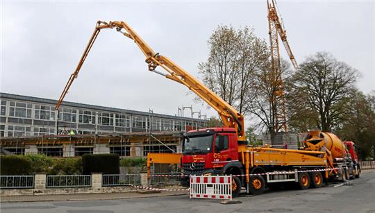 Betonmischer und Betonpumpe stehen vor einem Gebäude.