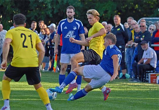 Fußballspieler in gelber und blauer Trikots in Aktion auf dem Spielfeld vor Zuschauern und einer Auswechselbank