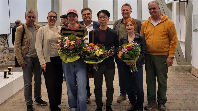 Das Bild zeigt den Gewinner des Andreaspreises 2026 Ryo Kato (Mitte), die Zweitplatzierte Ute Vauk-Ogawa (r.) und die Drittplatzierte Silke Hermanni (l.), umgeben von Jury und Laudatoren.