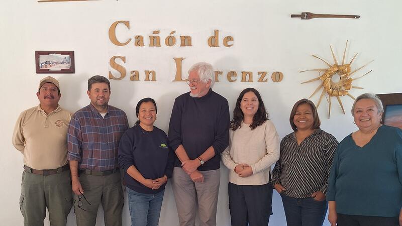 Eine Gruppe von Menschen steht vor einer Wand, auf der in goldenen Buchstaben Cañón de San Lorenzo steht.