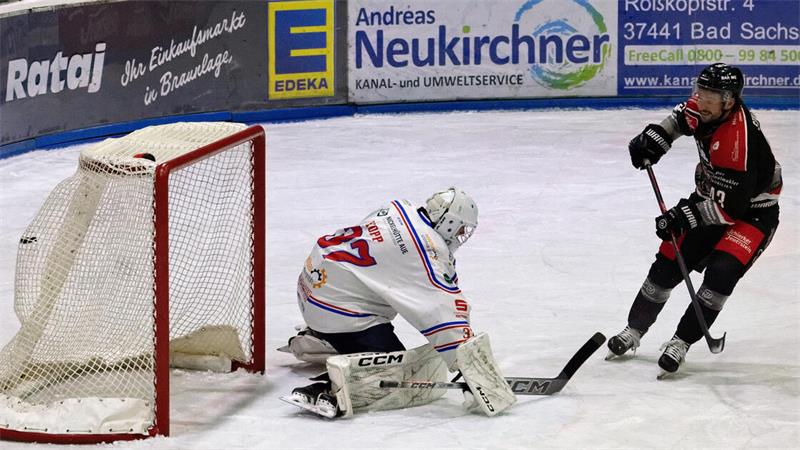 Eishockeyspieler in schwarzer Ausrüstung mit Stock vor Torwart in weißer Ausrüstung auf dem Eis