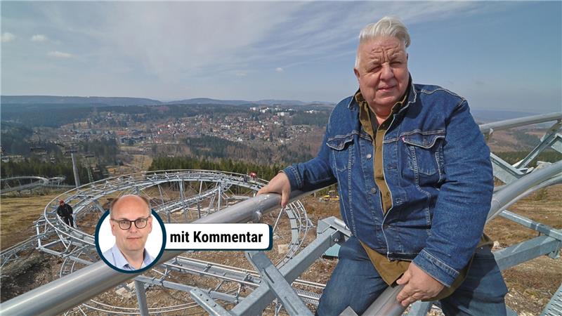 Person mit Jeansjacke lehnt an einem Metallgeländer mit Blick auf eine kurvige Sommerrodelbahn und eine Stadt im Hintergrund