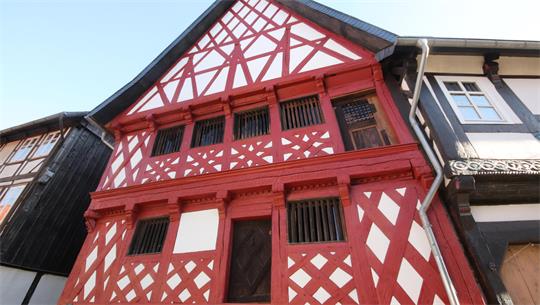 Fachwerkhaus mit rot-weißem Fachwerk und mehreren Fenstern unter einem spitz zulaufenden Dach