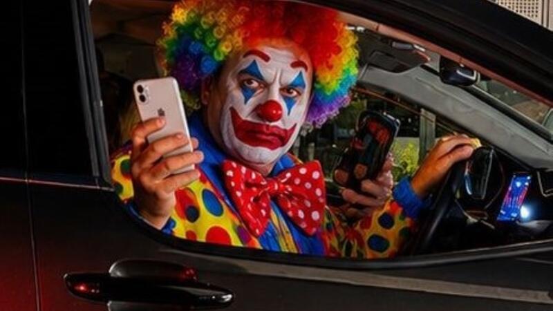 Auf dem mit KI-generierten oder bearbeiteten Bild ist ein Clown in einem Auto zu sehen, der mit einem Handy aus einem Auto fotografiert.
