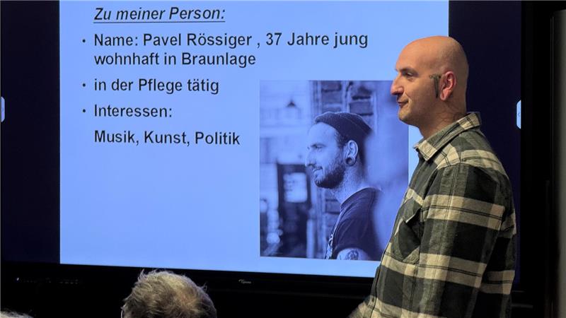 Ein Mann steht vor einem Bildschirm, auf dem er auch zu sehen ist.