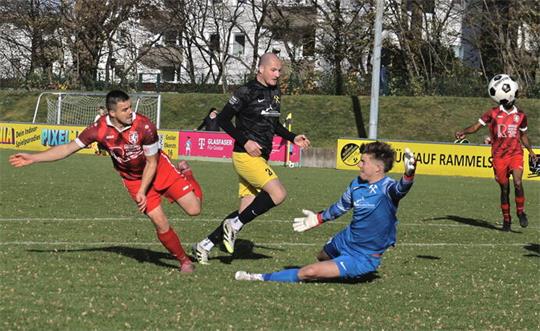 Fußballspiel mit mehreren Spielern in Aktion auf einem Spielfeld, ein Spieler in blau rutscht zum Ball, andere Spieler tragen rote und schwarze Trikots