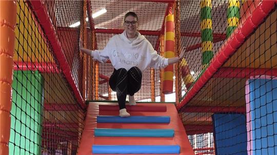 Kind klettert auf einer bunten Indoor-Spielplatzrutsche mit Netzumzäunung.