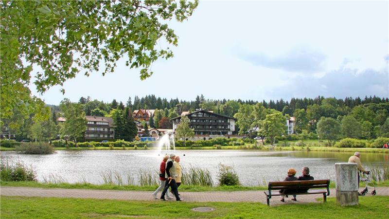 Märchentante, Hase und Förster geben sich die Klinke in die Hand Spaziergänger gehen um einen Teich mit Fontäne. Menschen sitzen auf einer Bank.