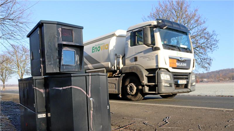 Blitzeranhänger am Straßenrand, ein Lkw fährt vorbei.